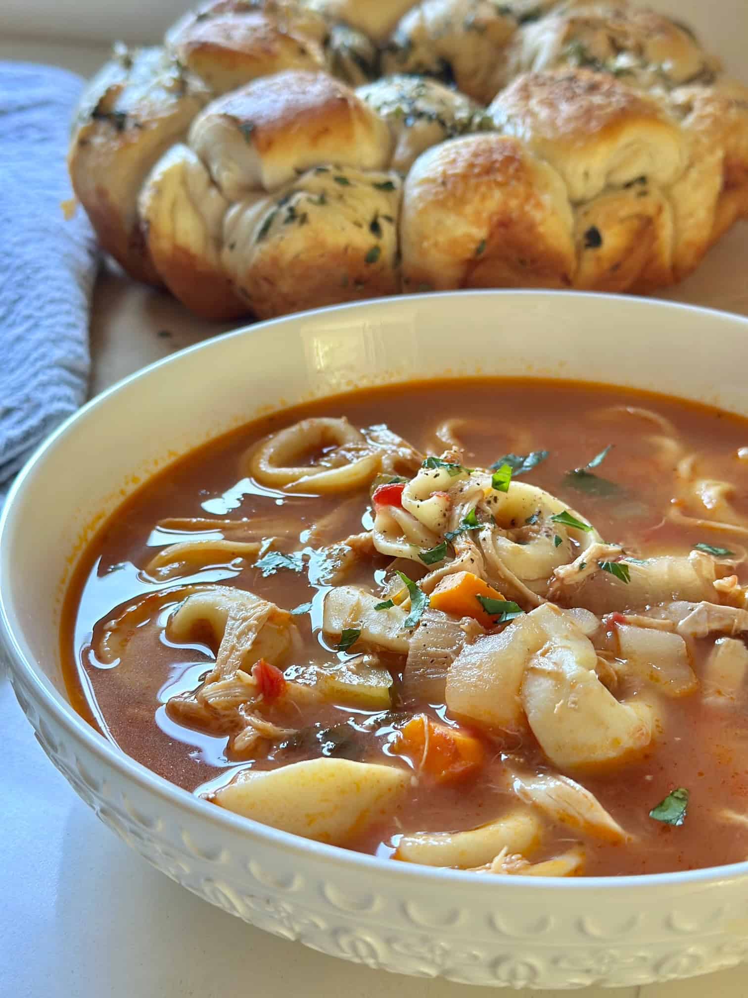The soup in a bowl with herb pull apart bread in the background. 