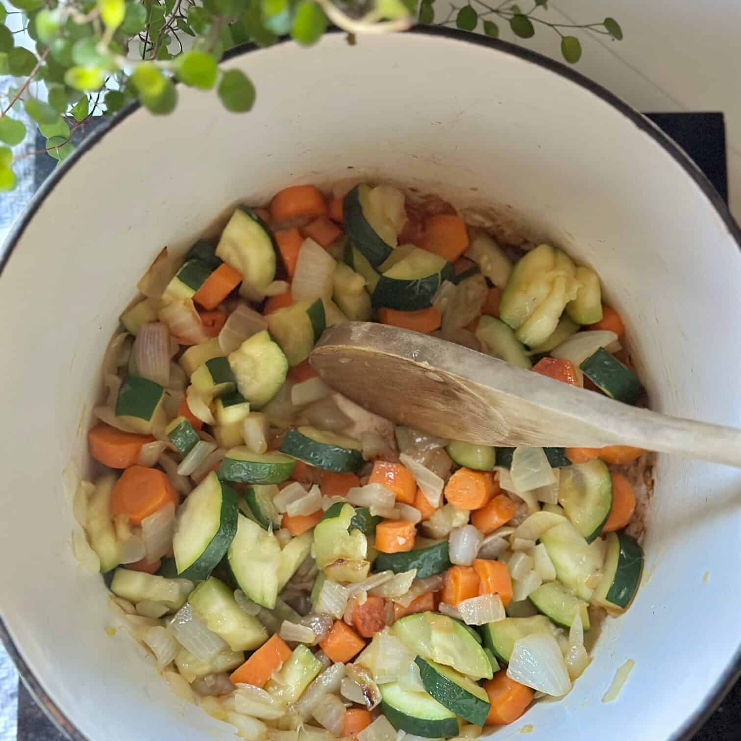 Carrots, onions and zucchini sautéing in a white pot. 