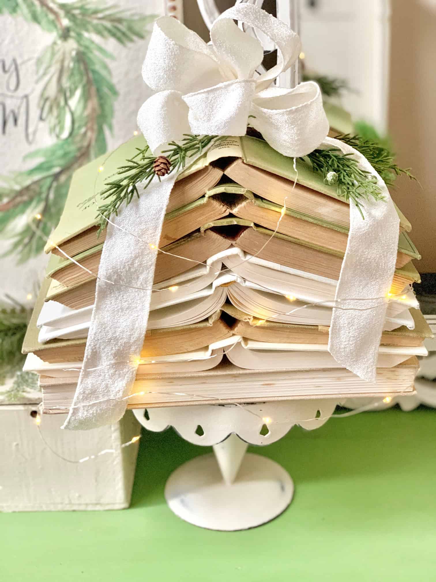 A stack of neutral covered books, stacked as a Christmas tree on top of a vintage cake stand.