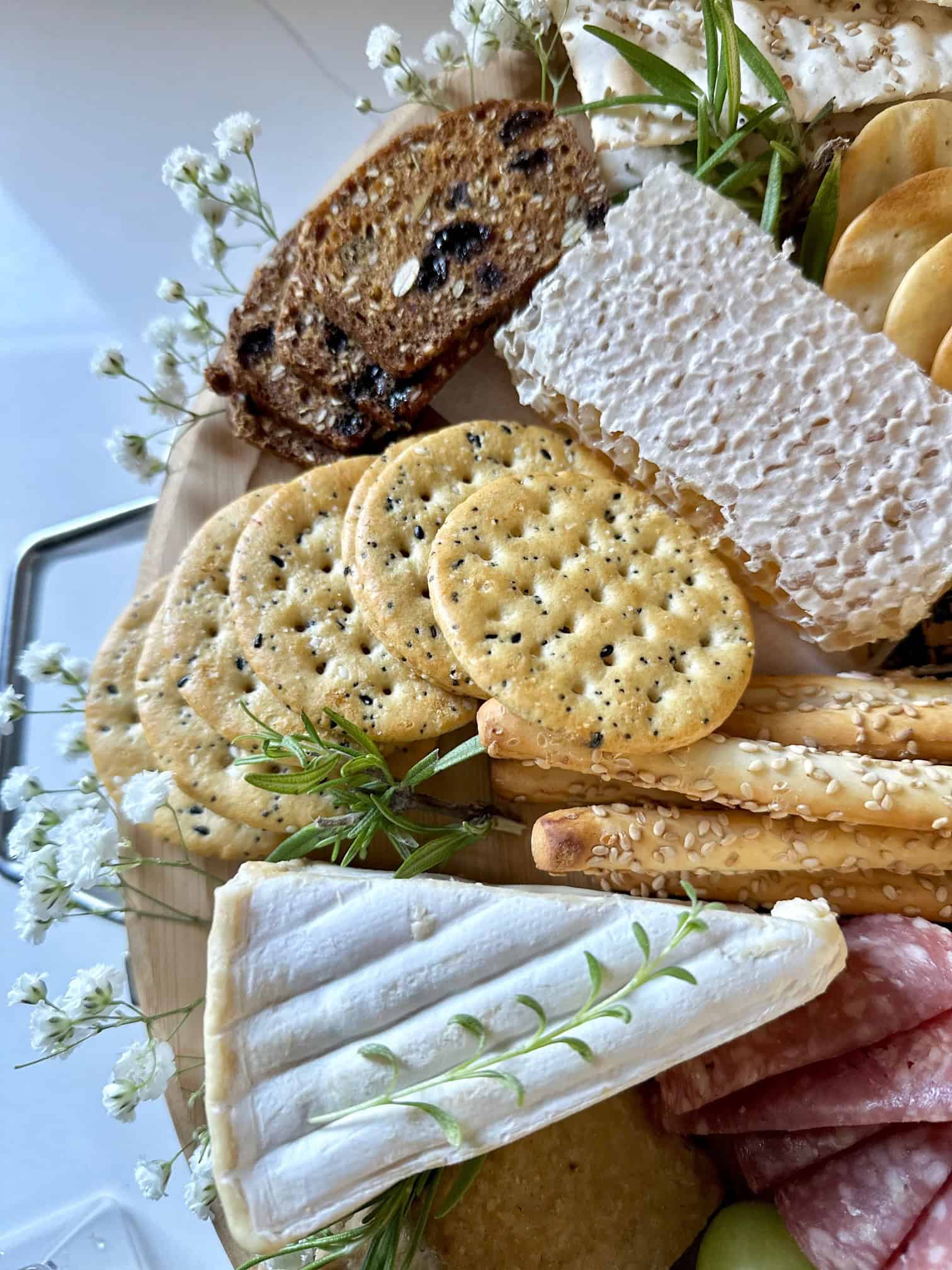 Side of charcuterie board with honeycomb, cheese, crackers and flowers.