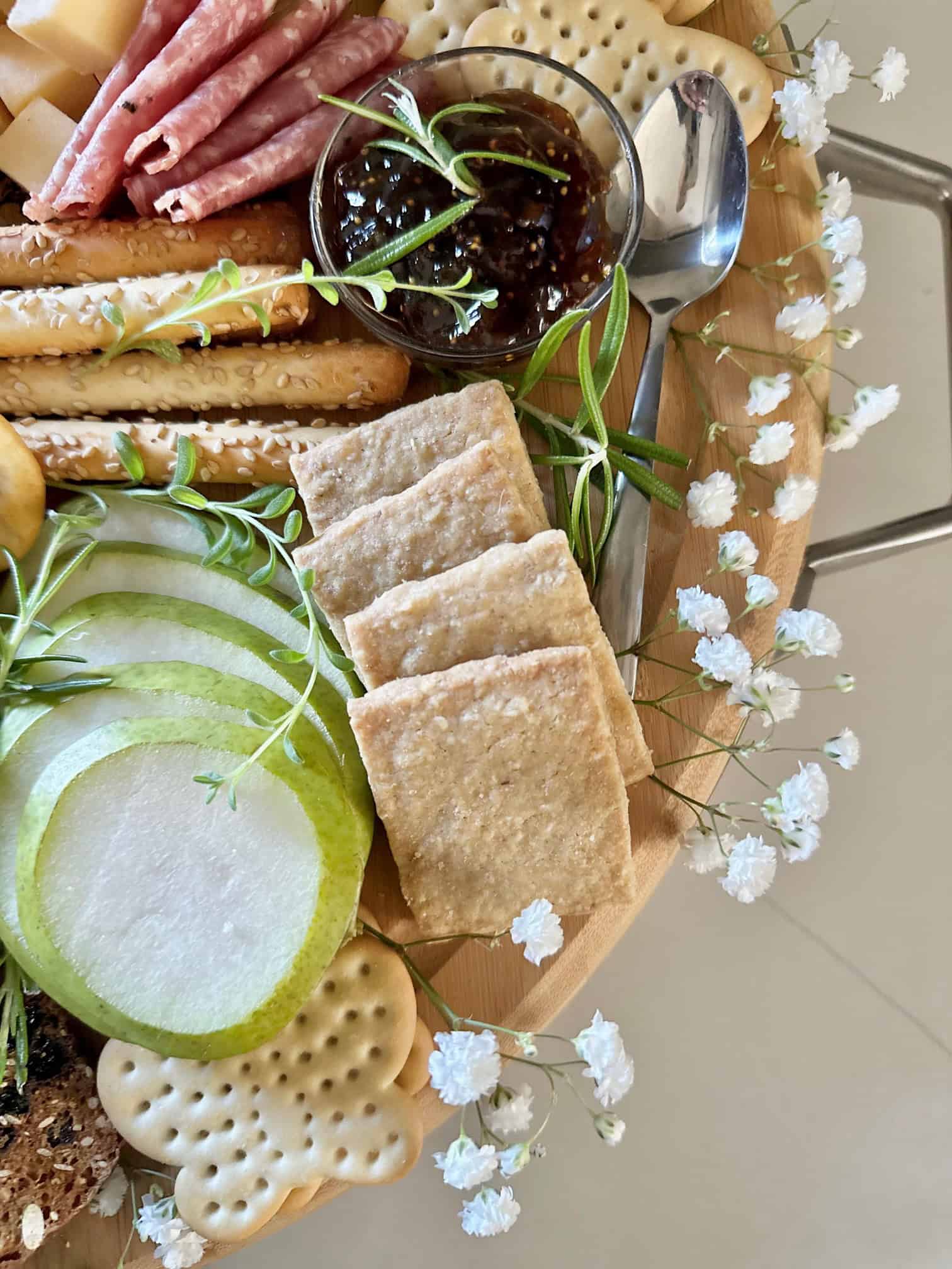 Close up of an edge of a full charcuterie board with herbs and flowers. 