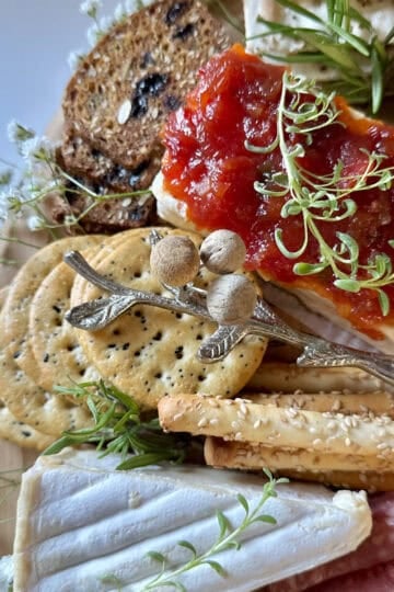 Cream cheese with pepper jelly dip on a charcuterie board with crackers.