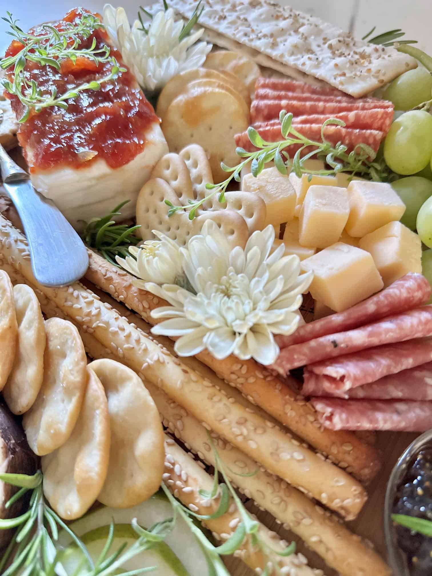 Crackers, cheeses, flowers and herbs on a board. 