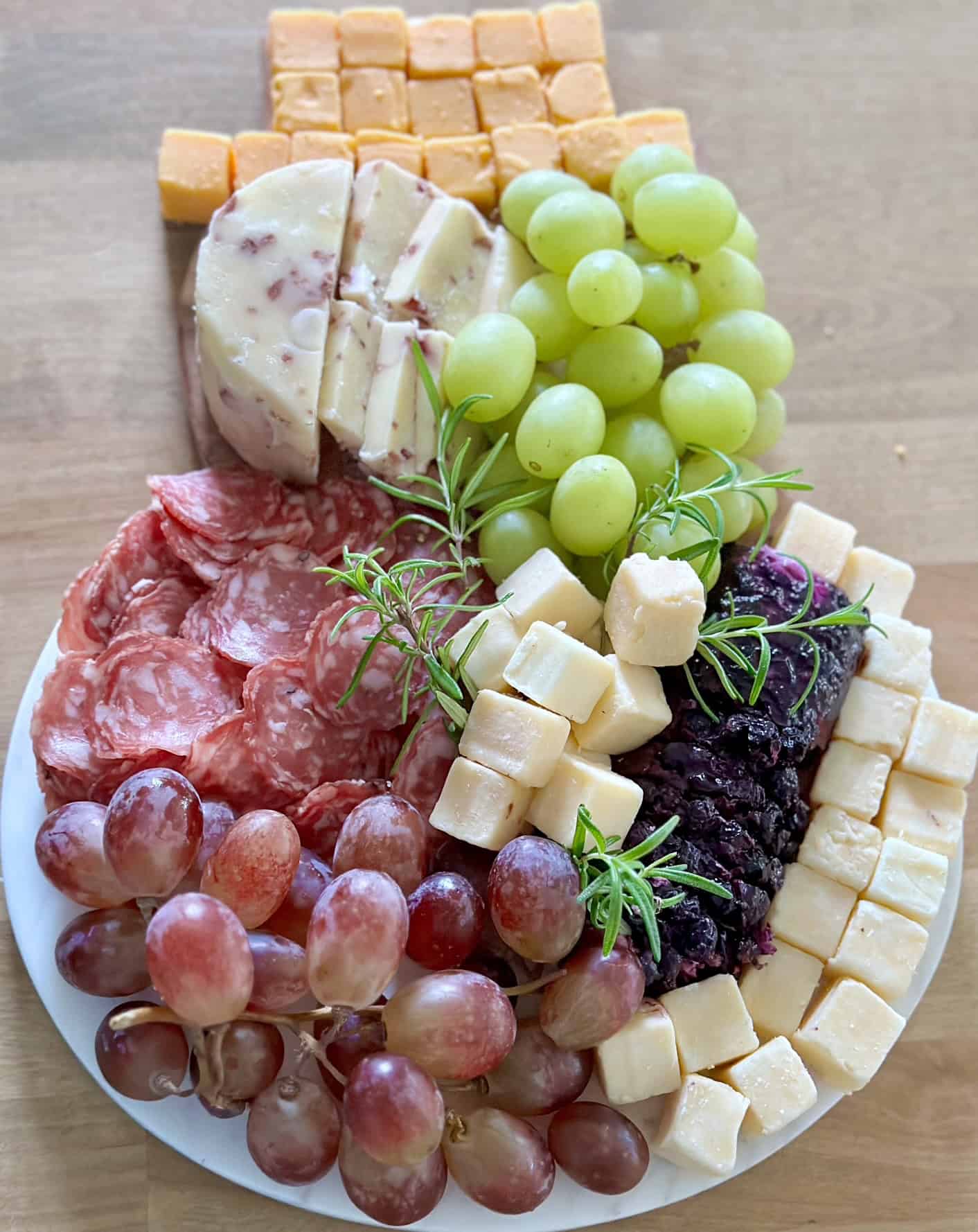 Snowman shaped charcuterie board with cubed cheese, grapes and rosemary for garnish. 