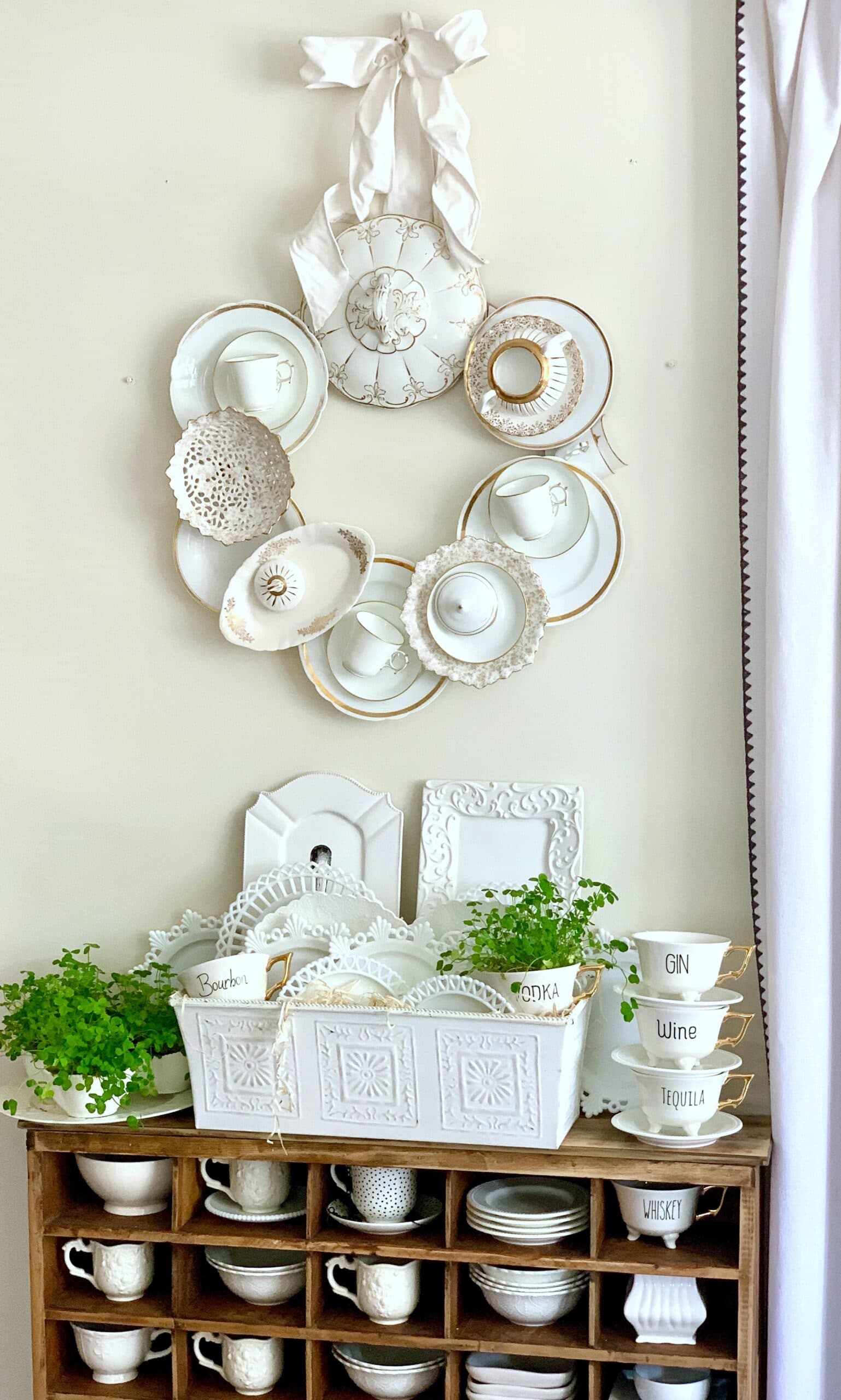 My china wreath with a cubby below. on the cubby are tea cups with various alcohol names. The tea cups have shamrocks in them. 