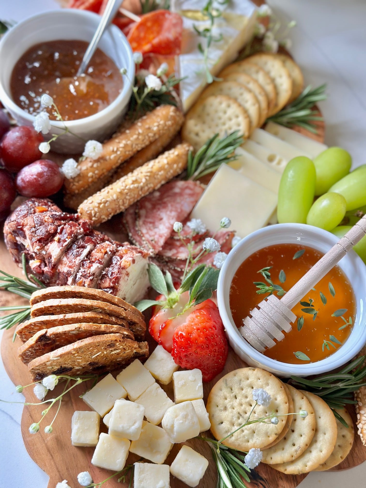 A full charcuterie board with meat, cheeses, crackers, fruits and jams. 
