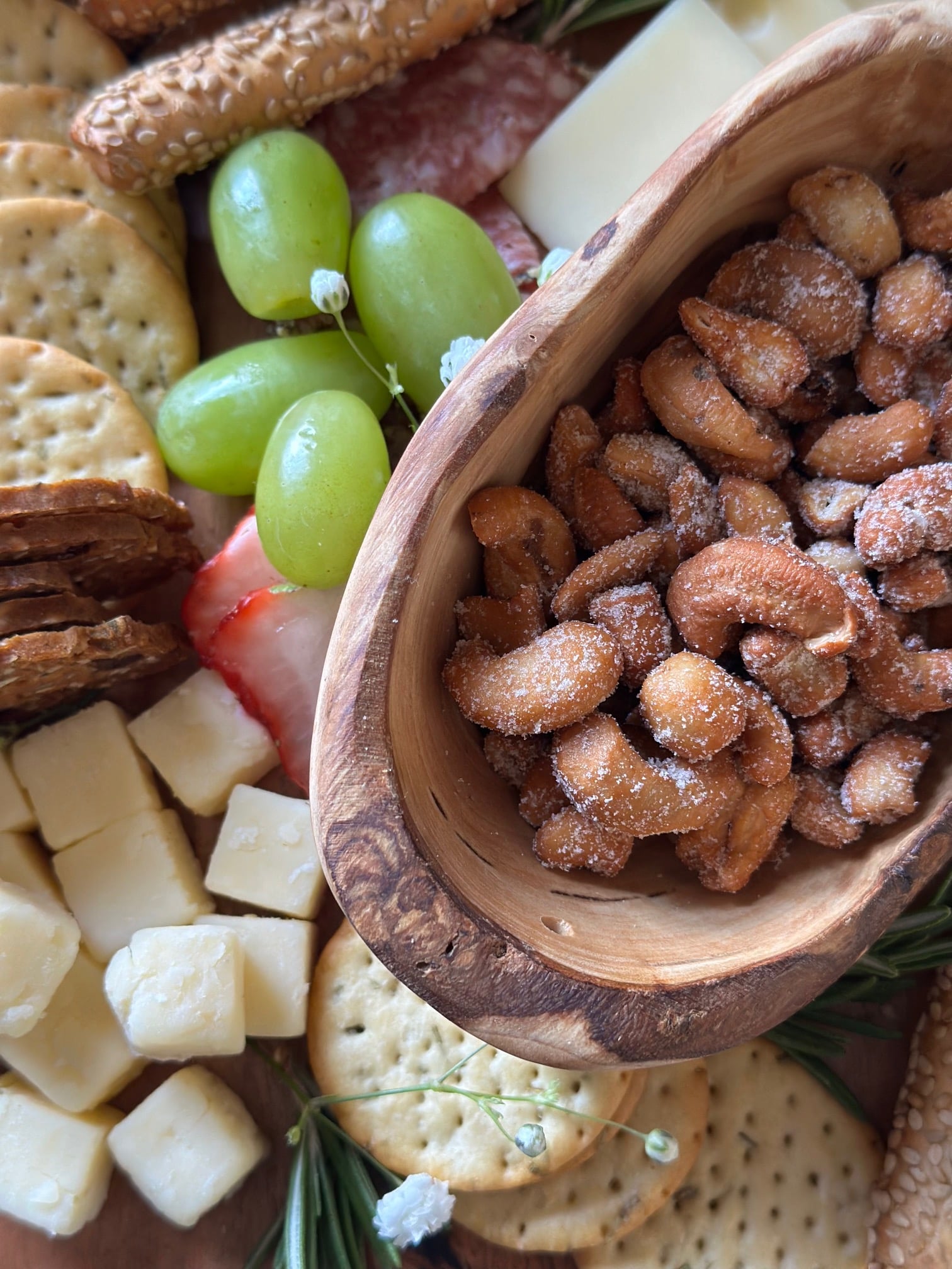 Cashews in a small wood bowl on a charcuterie board. 