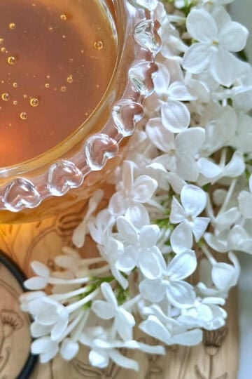 Lilac honey in a honey jar with fresh white lilac next to it.