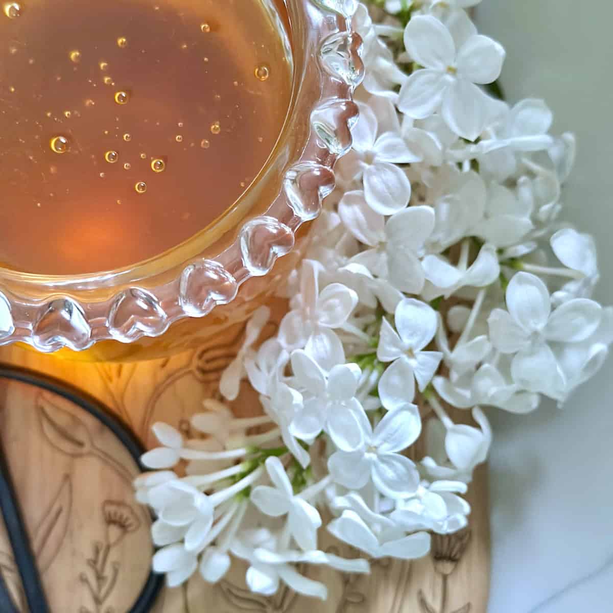Lilac honey in a honey jar with fresh white lilac next to it.