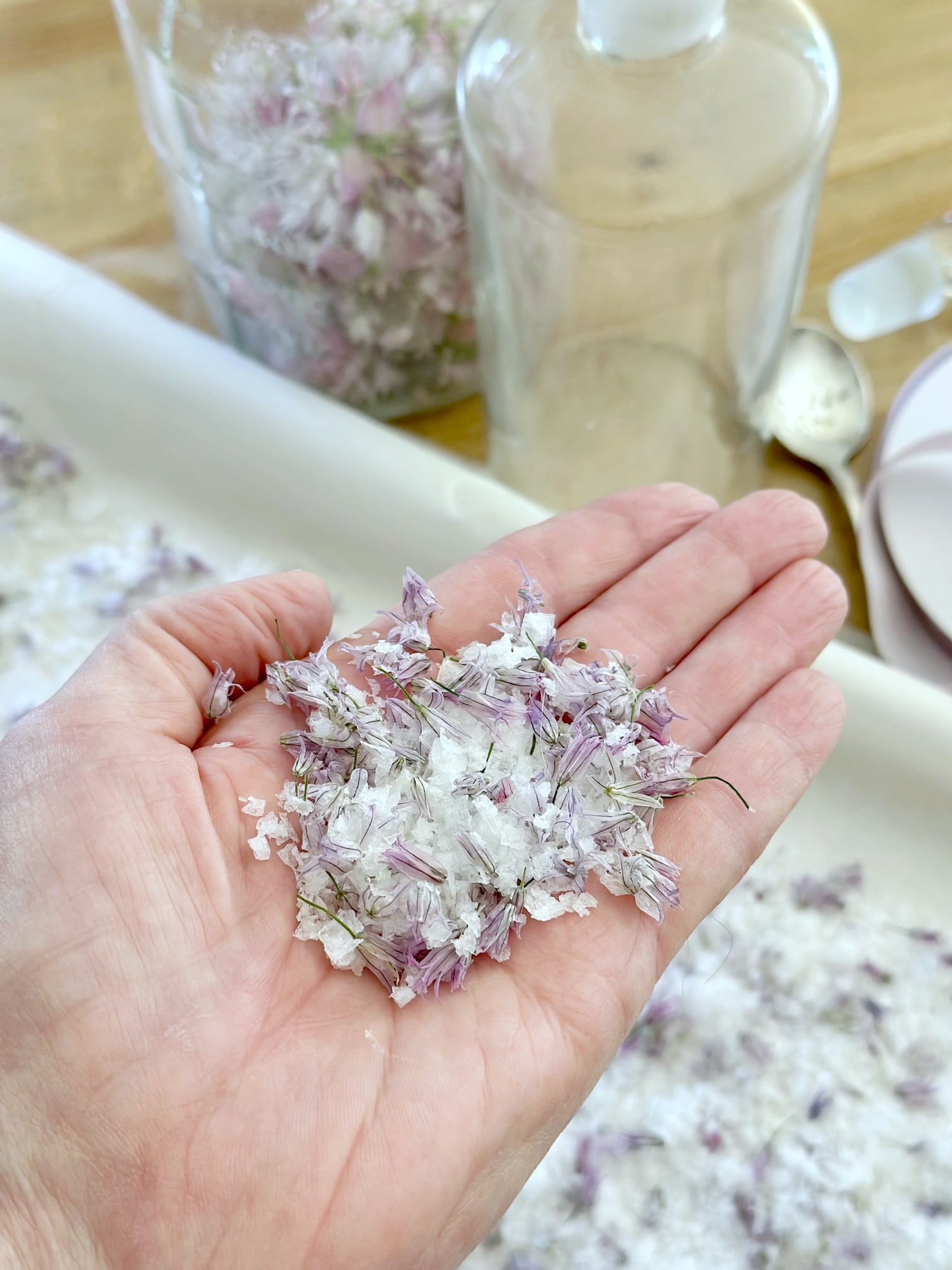 My hand holding some chive flower salt over a pan.
