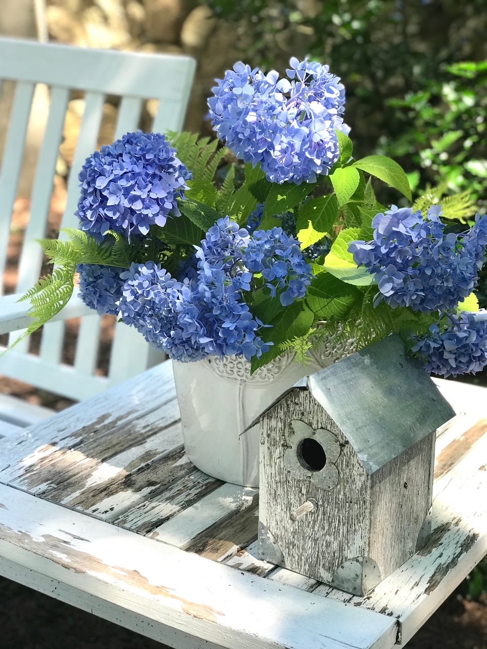 Hydrangea stems in a vase near a birdhouse.