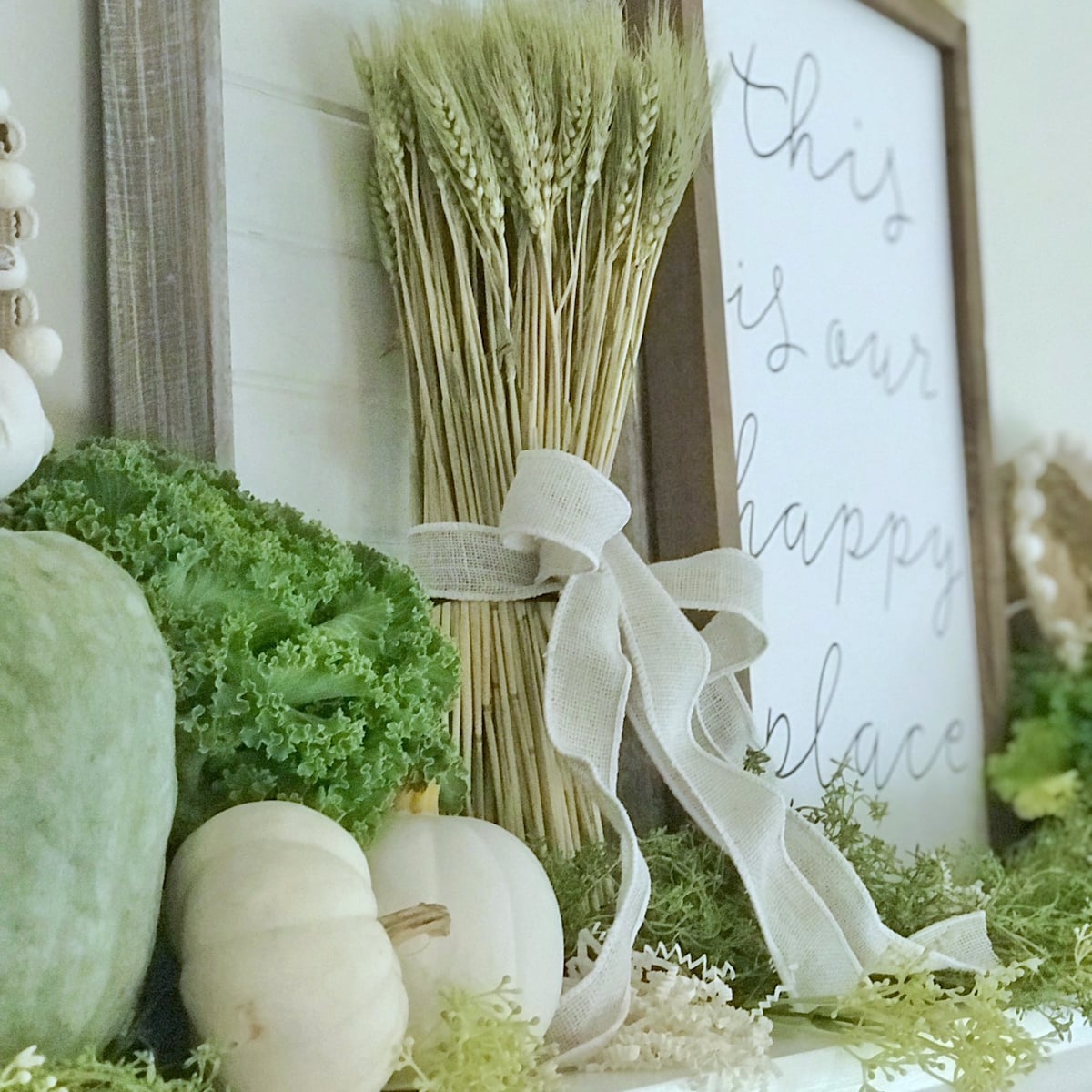 White pumpkins on a mantel with kale, green pumpkins and lots of fall fillers. 