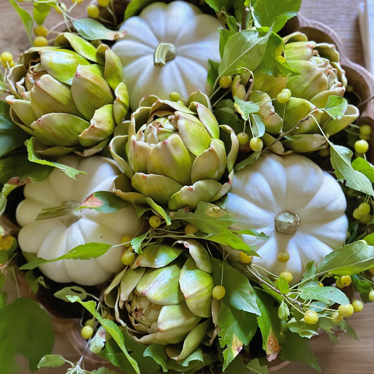 White mini pumpkins with faux artichokes in a wooden bowl. 