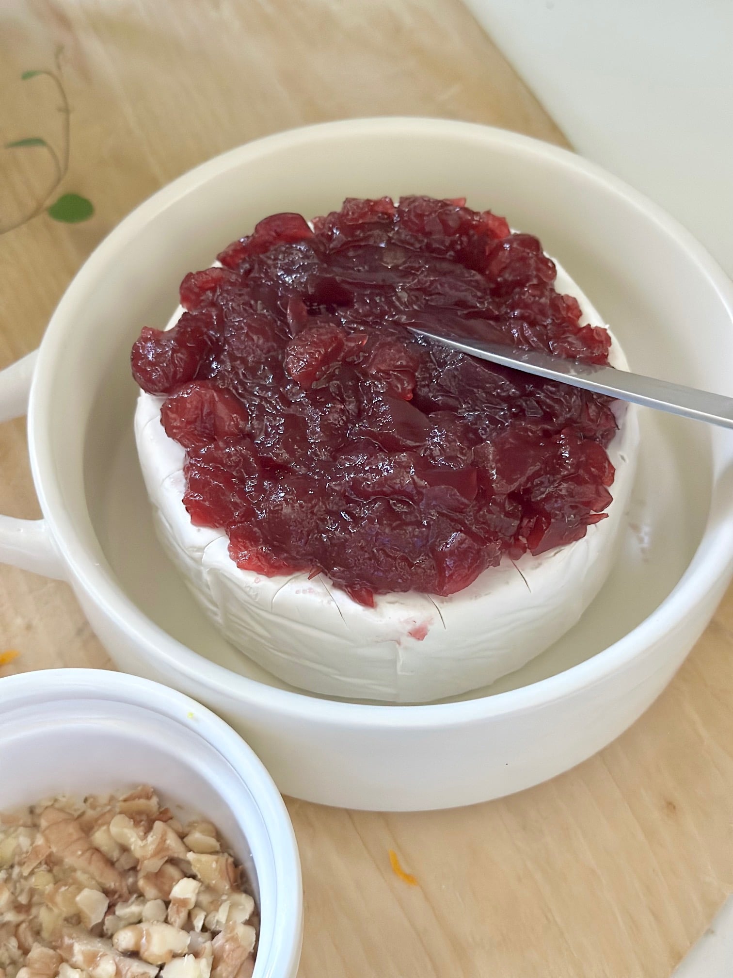 Adding cranberry on top of a wheel of brie.