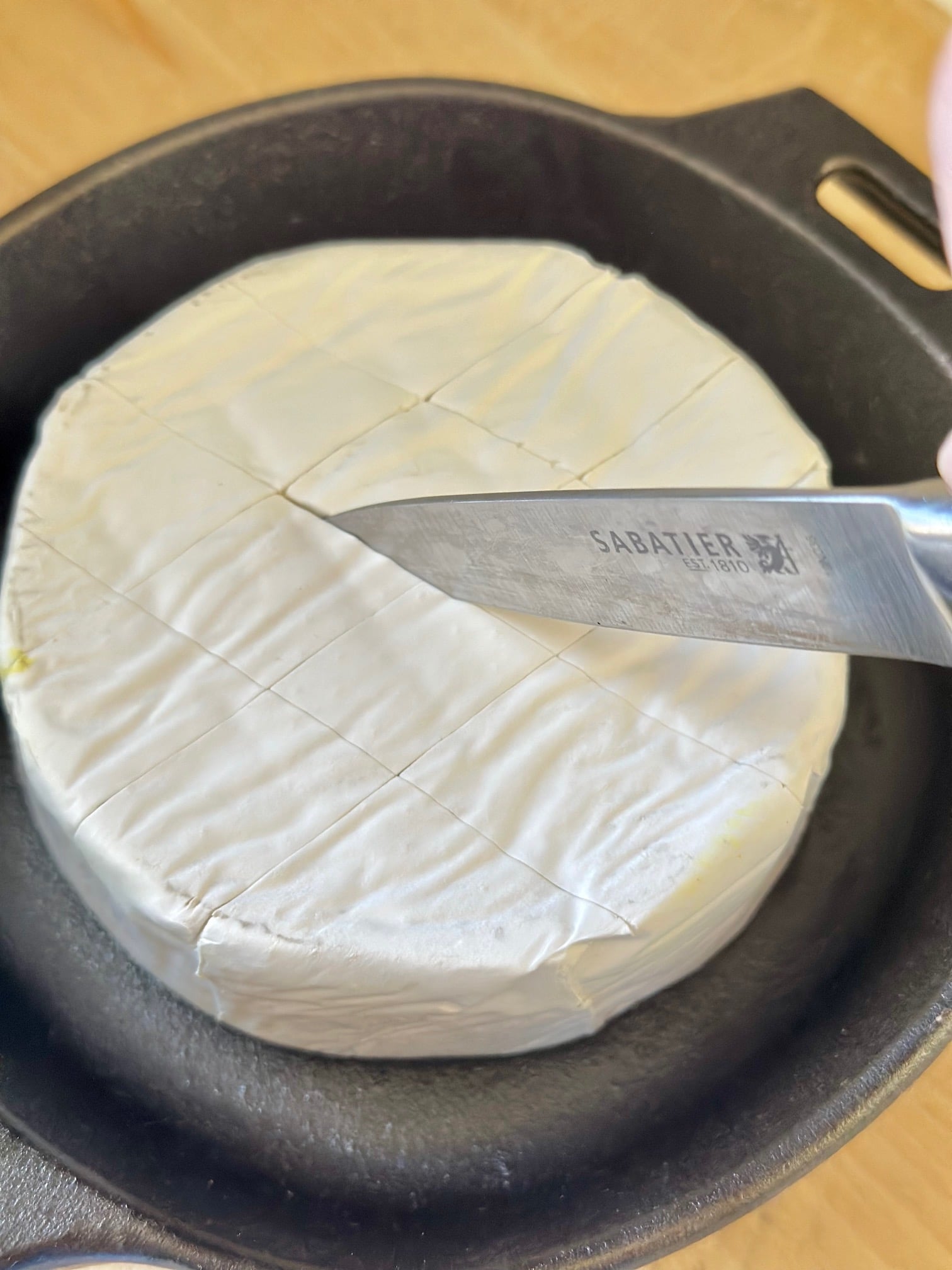 scoring the top of a wheel of brie with a knife. 