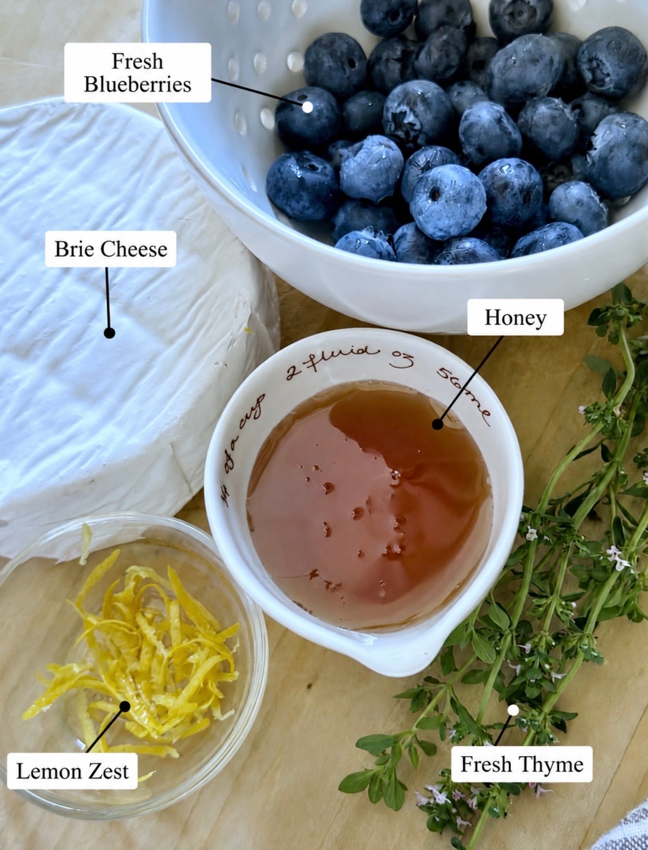 Ingredients for blueberry baked brie including fresh blueberries, brie, lemon zest, honey and fresh sprigs of thyme. 