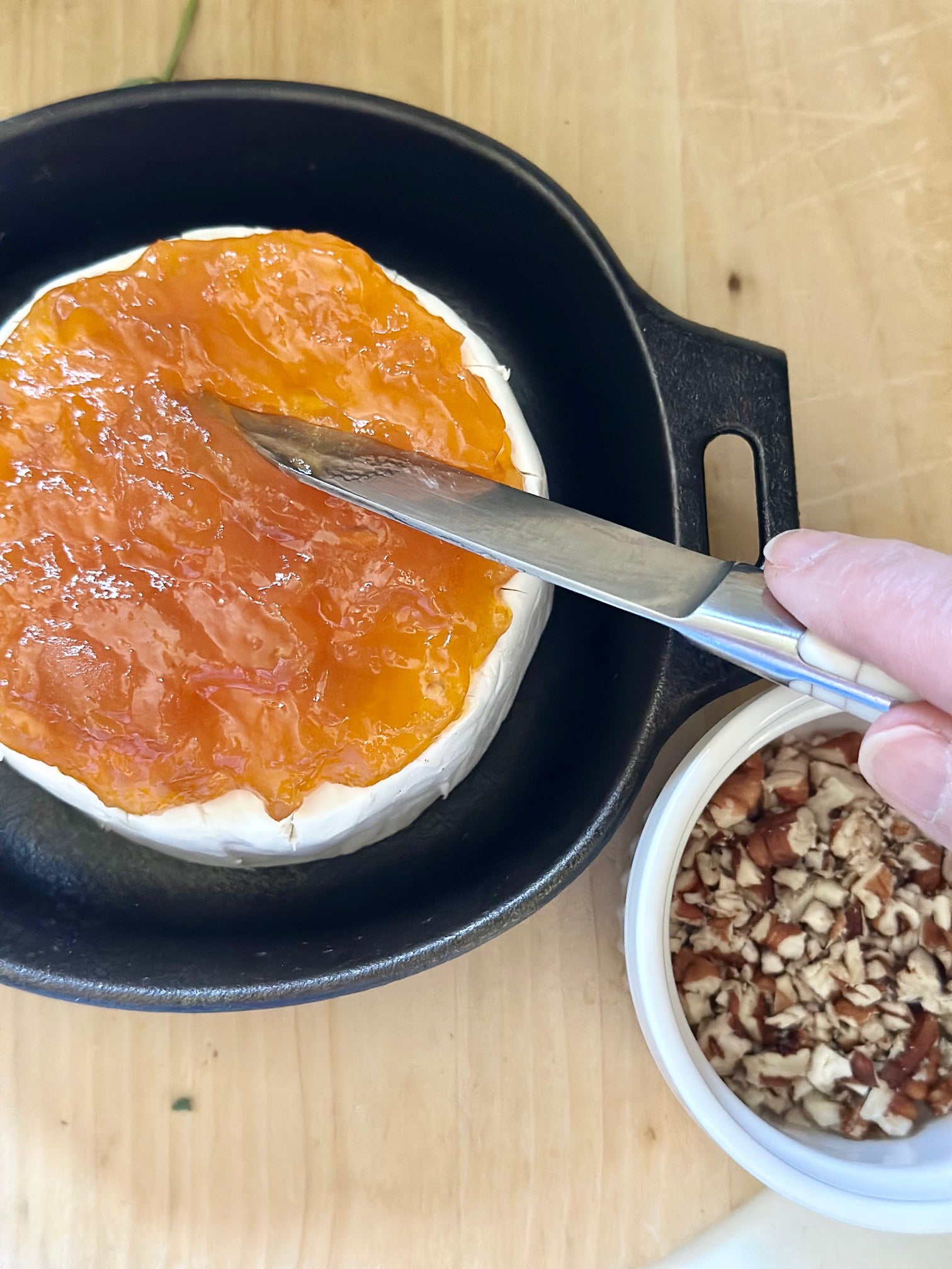 Spreading apricot preserves on the wheel of brie. 
