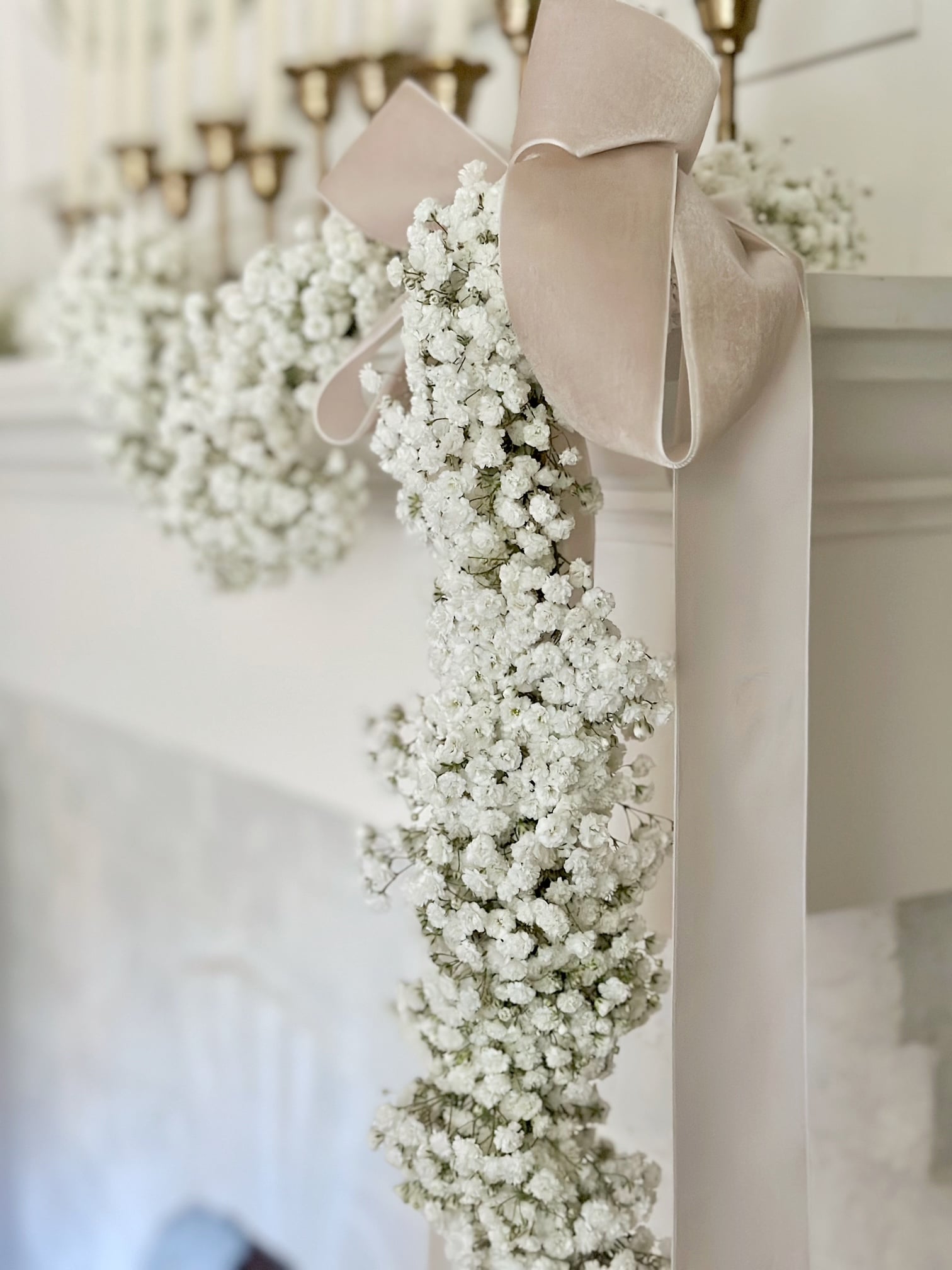 A stunning full babies breath garland hanging from our mantel. At the corner is a bow made of soft pink velvet ribbon.