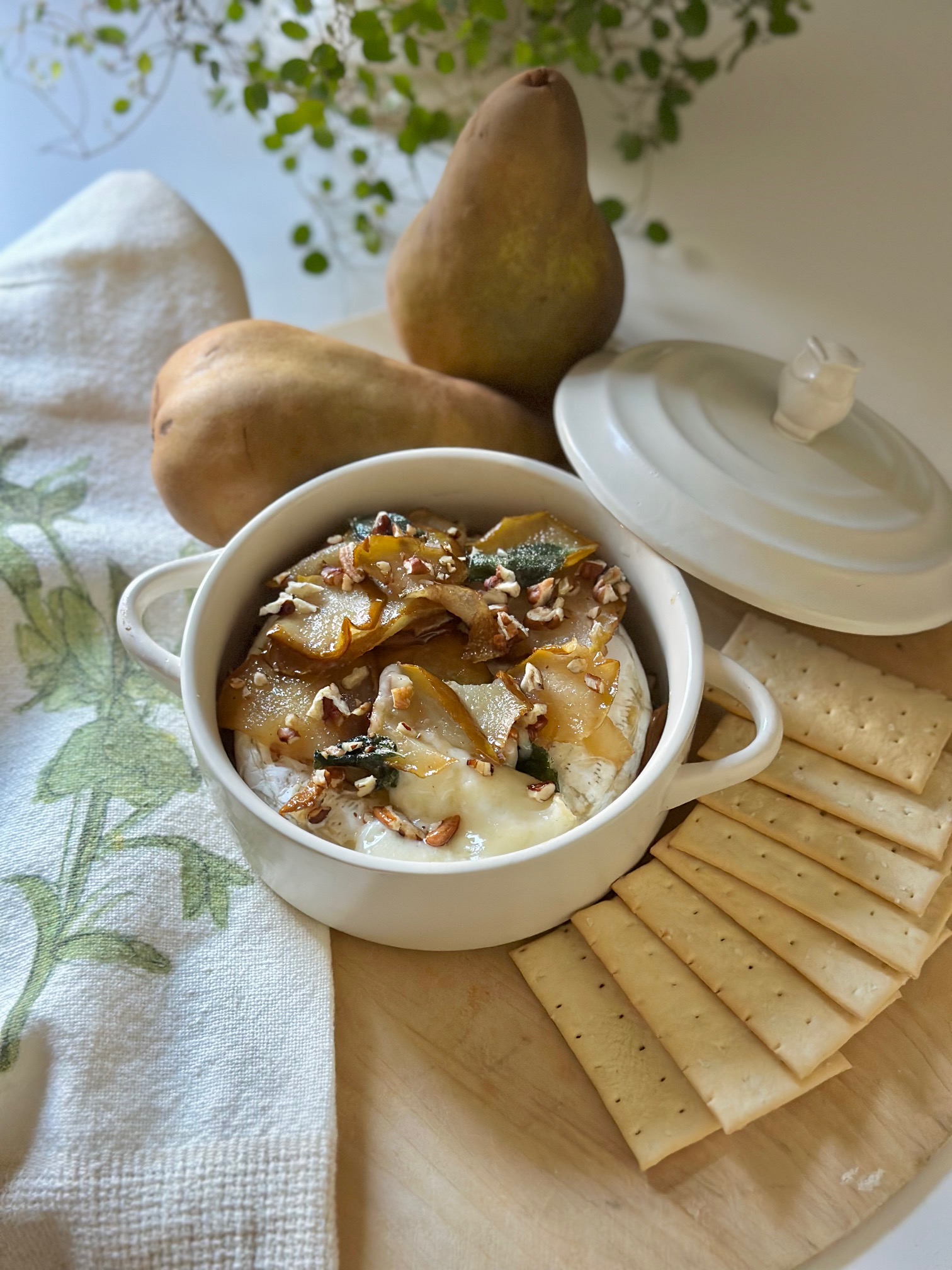 Baked brie with pears on a serving board with crackers.